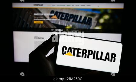 Persona che possiede uno smartphone con il logo della società statunitense di attrezzature pesanti Caterpillar Inc. Sullo schermo davanti al sito Web. Concentrarsi sul display del telefono. Foto Stock