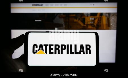 Persona che possiede un telefono cellulare con il logo della società americana di attrezzature pesanti Caterpillar Inc. Sullo schermo davanti alla pagina Web. Concentrarsi sul display del telefono. Foto Stock