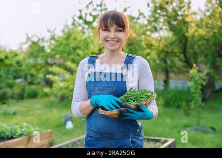 Ritratto di donna contadina sorridente con cestino di erbe rucola guardando la macchina fotografica Foto Stock