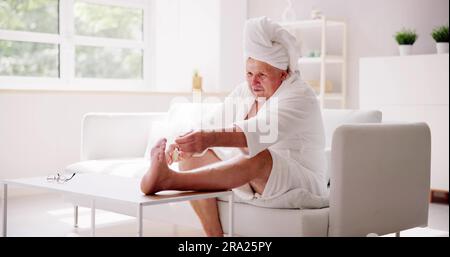 Divertente uomo che si rilassa in accappatoio facendo pedicure Spa a casa Foto Stock