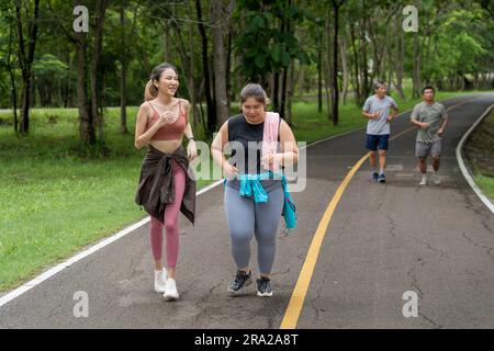 Due giovani donne, magre e sovrappeso, si divertono l'una con l'altra durante la loro corsa mattutina su una pista da corsa di un parco locale Foto Stock