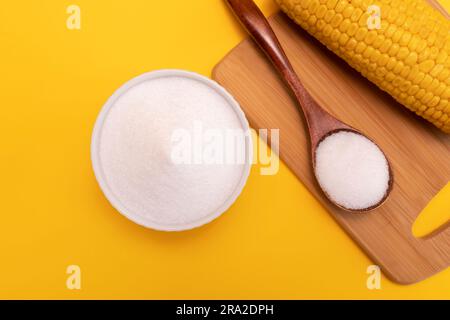 Dolcificante naturale eritritolo, prodotto per fermentazione da mais in recipiente di ceramica, cucchiaio di legno, pannocchia di mais su sfondo giallo arancio. Sostituto dello zucchero Foto Stock