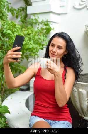 Ritratto di una donna ucraina sorridente che beve un cappuccino caldo e scatta un selfie Foto Stock