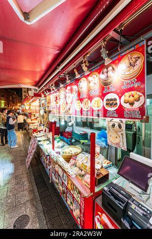 Scena di strada notturna lungo una fila di bancarelle di cibo cinese che vendono cibi cinesi come gnocchi e panini in streaming nella popolare Chinatown di Kobe. Foto Stock