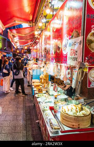 Scena di strada notturna lungo una fila di bancarelle di cibo cinese che vendono cibi cinesi come gnocchi e panini in streaming nella popolare Chinatown di Kobe. Foto Stock