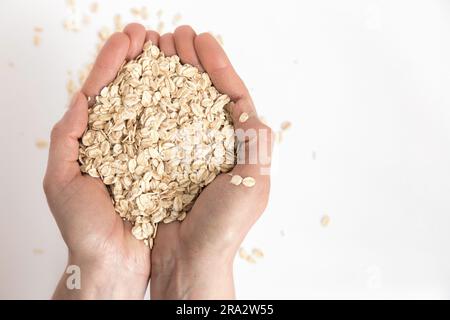 Mani piene di fiocchi d'avena su sfondo bianco. Alimenti super ricchi di sostanze nutritive che possono essere utilizzati per diverse ricette. Mangiare sano. Vista dall'alto e copia Foto Stock