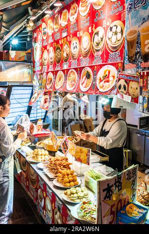 Donna che serve una giovane donna in una bancarella cinese che vende cibi su un bastone, gnocchi e panini al vapore. Notte a Chinatown, Nankinmachi, Kobe. Foto Stock