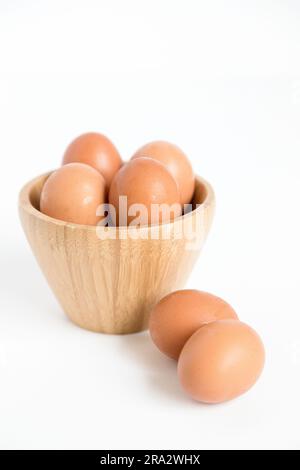 Diverse uova di gallina fresche poste dentro e fuori un contenitore di bambù su sfondo bianco. Copia spazio. Foto Stock