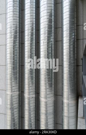 Tubi di ventilazione che salgono fino al tetto sulla parete esterna di un edificio alto Foto Stock