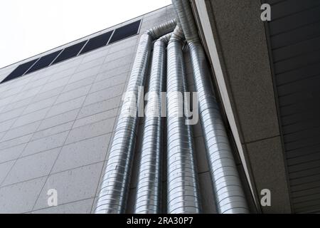 Tubi di ventilazione che salgono fino al tetto sulla parete esterna di un edificio alto Foto Stock