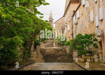 Una storica strada residenziale nella città di Nerezisca sull'isola di Brac in Croazia. La Chiesa di nostra Signora del Carmelo è sullo sfondo Foto Stock