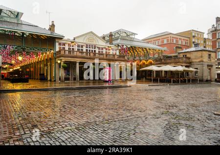 Il popolare mercato di Covent Garden di Londra in una giornata di pioggia con union Jack e bandiere inglesi appese sopra i negozi. La cabina telefonica Love è un sito raro a Londra Foto Stock