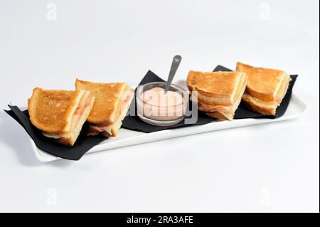 Club sandwich, avvolto in eleganti tovaglioli neri, composto da molti gustosi ingredienti, con un barattolo di salsa, su un piatto bianco e su fondo. Foto Stock