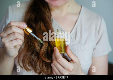 Giovane donna che applica olio essenziale biologico naturale sui capelli. Centro benessere e rituali di bellezza. Cura della pelle Foto Stock