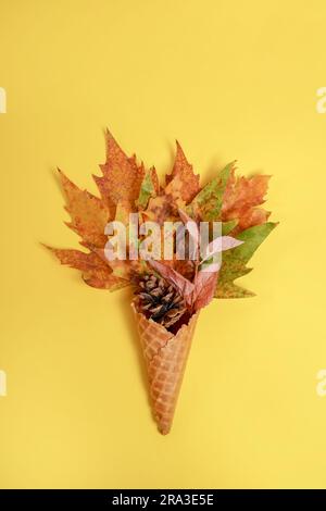 Cono gelato ripieno di foglie di acero autunnale su sfondo giallo Foto Stock