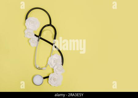 Stetoscopio e fiori di carta bianca su sfondo giallo. Giorno del Dottore nazionale. Buon giorno dell'infermiera, biglietto d'auguri con spazio per le copie Foto Stock