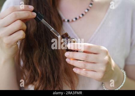 Giovane donna che applica olio essenziale organico naturale su capelli e pelle. Centro benessere e rituali di bellezza. Cura della pelle. Foto Stock