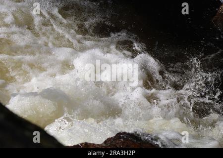 Un primo piano di acqua che cade sulle rocce in un fiume che scorre velocemente Foto Stock