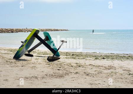 Due tavole kitesurf appoggiate sulla sabbia della spiaggia con un kitesurf surf sullo sfondo. Concetto di sport acquatici Foto Stock