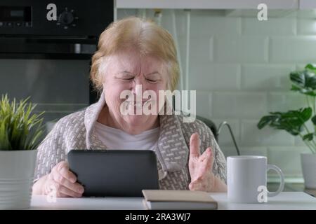 Donna anziana felice con un tablet digitale che videochiama a casa Foto Stock