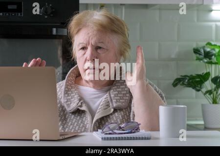 Scioccata donna anziana a casa che guarda un notebook che vede cattive notizie Foto Stock