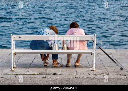 due donne anziane in pensione o donne sedute su una panchina insieme al mare. due nonne sedute su una panchina al mare a chiacchierare. Foto Stock