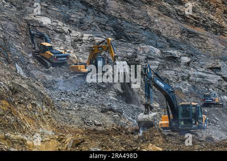 Gli escavatori Hyundai rompono le rocce e rimuovono i detriti dopo una frana lungo la National Highway 150 dopo una forte pioggia monsonica alla periferia di Churachandpur, Manipur Churachandpur si trova in una regione collinare ed è soggetta a frane, soprattutto durante la stagione dei monsoni. Le forti piogge e i ripidi pendii in questa zona aumentano il rischio di frane. Fattori quali l’erosione del suolo, la deforestazione, l’uso improprio del suolo e le attività di costruzione possono anche contribuire al verificarsi di frane. Foto Stock