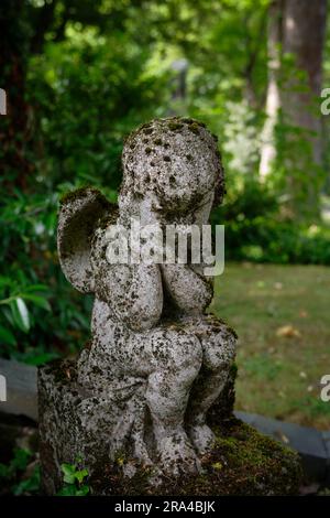 un piccolo e stanco putto mossy seduto su una tomba Foto Stock