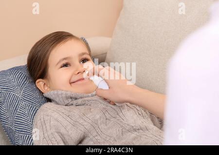 Madre che usa lo spray nasale per trattare la sua bambina sul divano, primo piano Foto Stock