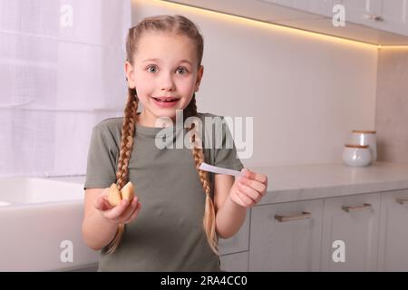 Una ragazza carina che tiene un gustoso biscotto della fortuna e legge le previsioni in casa. Spazio per il testo Foto Stock