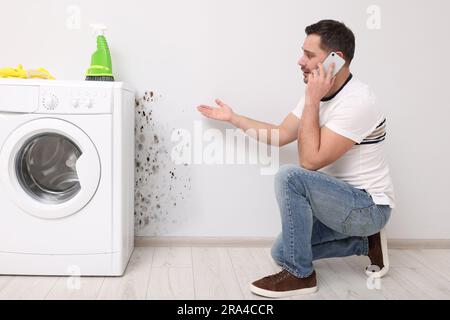 Servizio di rimozione dello stampo. Uomo che parla al telefono e guarda il muro interessato in bagno Foto Stock