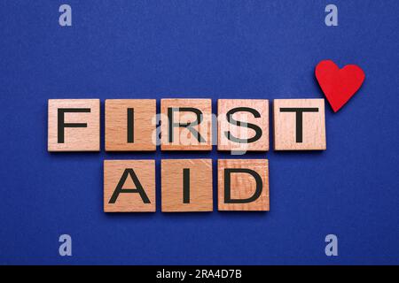 Parole pronto soccorso in cubi di legno e cuore di carta su sfondo blu, piatto Foto Stock