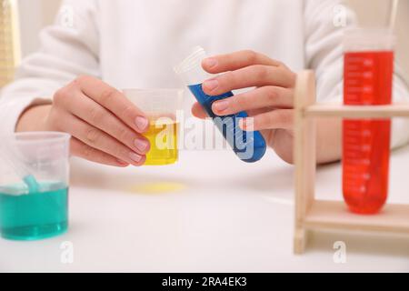 Ragazza che mescola liquidi colorati al tavolo bianco in interni, primo piano. Set di esperimenti chimici per bambini Foto Stock