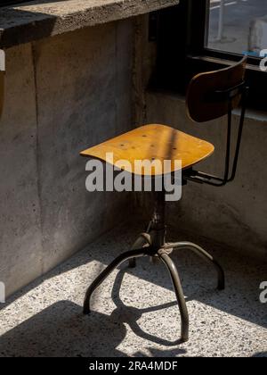 Schienale vuoto con sedie a filatura vintage, sedile rotondo decorato su sfondo muro di cemento, interni di un edificio in stile loft. Sedia girevole in legno, metà secolo Foto Stock