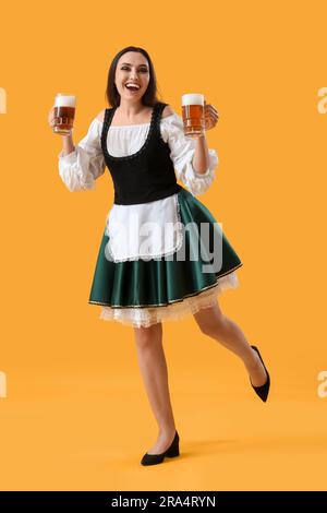 Bellissima cameriera dell'Octoberfest con birra che balla su sfondo giallo Foto Stock