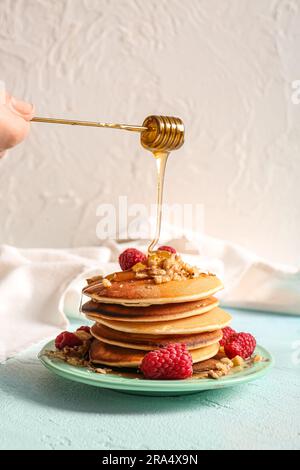 Aggiungere il miele ai gustosi pancake con lamponi su sfondo leggero Foto Stock