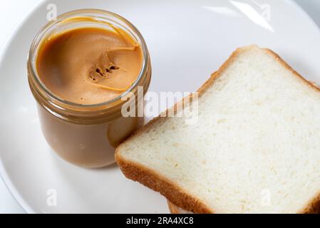 Un contenitore per barattoli di burro di arachidi cremoso con pane paglierino Foto Stock