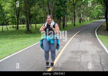 Giovane donna in sovrappeso che lavora al suo allenamento mattutino, corre su una pista da corsa di un parco locale Foto Stock