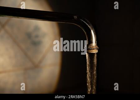 L'acqua fluisce da un vecchio rubinetto sporco al buio, su sfondo nero, in un punto di luce Foto Stock