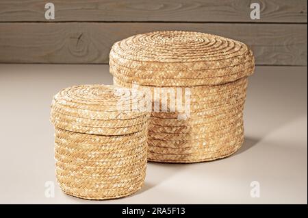 Due cestini - grandi e piccoli, tessuti in rattan, per riporre oggetti domestici su uno sfondo di legno. Foto Stock