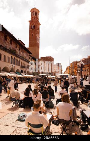 Persone sedute in Piazza delle Erbe, o piazza del mercato, Verona, Veneto Italia Europa, in primavera, sole a maggio. Viaggi e stile di vita in Italia Foto Stock