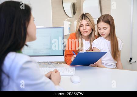 Madre del paziente firma modulo medico con lamentele e prescrizioni Foto Stock