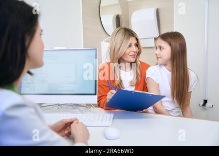 Donna che firma in forma di assicurazione dopo il check-up di salute della figlia Foto Stock