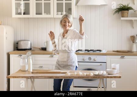 Una donna allegra e attiva e piuttosto matura che balla al tavolo della cucina Floury Foto Stock