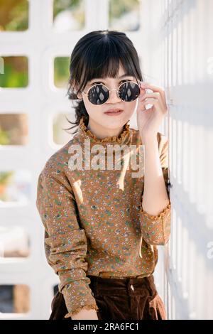 Occhiali da sole rotondi per adolescenti asiatici con abito vintage collezione moda estiva ritratto modello. Foto Stock