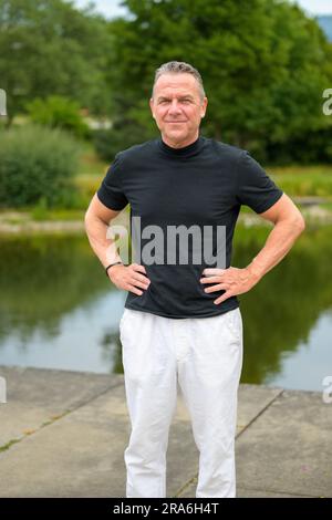 Ritratto di tre quarti di lunghezza di un attraente uomo anziano con le mani sui fianchi di fronte a un piccolo lago Foto Stock