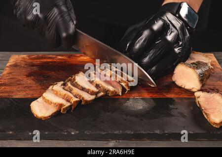 Lo chef taglia maiale alla griglia con coltelli da chef su un tagliere. Foto Stock