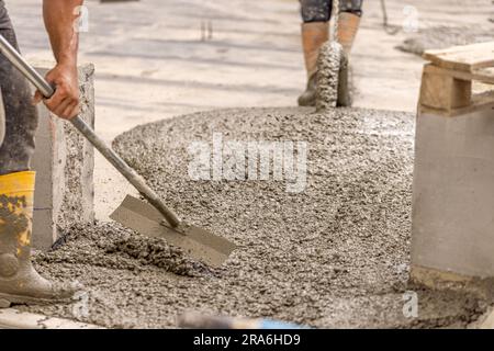 Il calcestruzzo di livellamento dei lavoratori versato dalla betoniera in cantiere Foto Stock