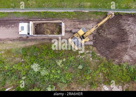 Vista aerea di un escavatore in funzione per rimuovere la terra e caricarla in un dumper su un cantiere edile. Foto Stock