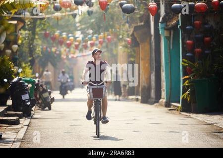 Escursioni in bicicletta nel centro storico. Strada della città antica decorata con lanterne tradizionali, Hoi An, Vietnam. Foto Stock